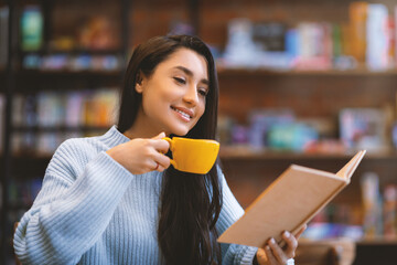 Young arab lady reading favorite book and enjoying coffee in cafe, sitting in cafeteria and...