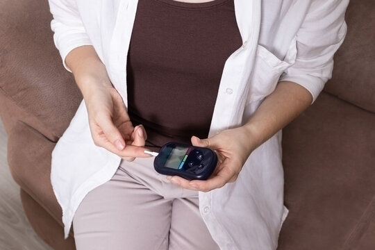 Close up of woman using glucometer to check blood sugar level. Concept of diabetes control, glucose monitoring, and healthcare routine.
