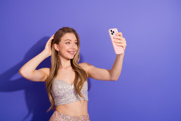 Elegant woman taking a selfie in stylish outfit against a purple background, expressing joy and...