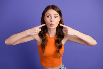 Cheerful and charming, playfully pointing at her puckered lips against a vibrant violet backdrop