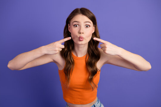 Cheerful and charming, playfully pointing at her puckered lips against a vibrant violet backdrop