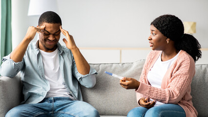 Confused black lady showing her stressed boyfriend positive pregnancy test, home interior, copy...