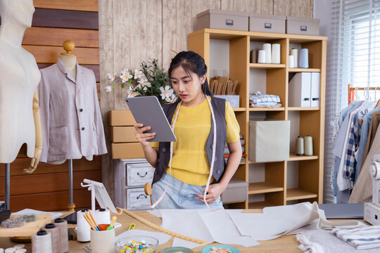 Small business fashion tailor, woman creative clothing workshop sewing boutique, Female designer uses tablet to review garment sketches, balancing digital tool with fabric planning in clothes business