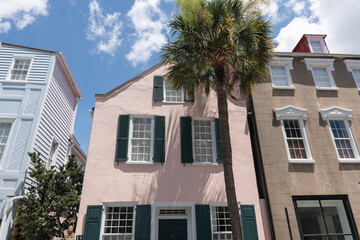 Charleston, South Carolina, USA - July 2, 2025. A pastel pink rowhouse with green shutters and palm tree in front.