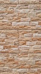 Vertical pattern of rectangular beige and brown stone tiles with natural texture forming a stacked wall surface. Architectural cladding material photography. 