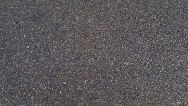 Close-up of black asphalt road surface with rough granular texture and visible stone aggregate. Urban pavement material photography. Infrastructure and construction background concept