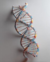 A stylized 3D rendering of a DNA double helix, composed of small, colorful particles, against a neutral background.  The helix shows multiple turns, exhibiting a textured, granular appearance