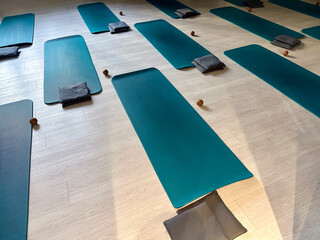 Yoga or pilates studio with neatly arranged teal mats, gray cushions, and small wooden massage...