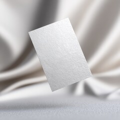 A subtly textured, off-white rectangular card floats above a softly draped, light beige fabric backdrop