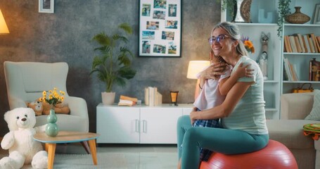 Happy little daughter hugging her pregnant mother sitting on fitness ball during home workout in living room, symbolizing love, family bonding, and joyful maternity lifestyle. - Powered by Adobe