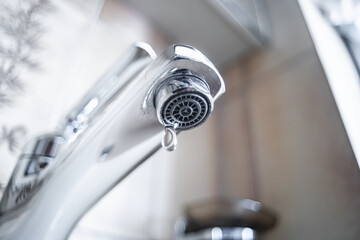 Dripping tap with water droplets inside apartment bathroom.