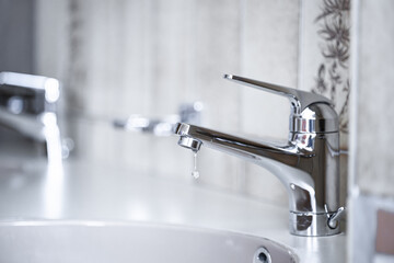 Dripping tap with water droplets inside apartment bathroom. Macro, close up shot, shallow depth of field, no people