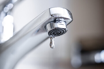 Dripping tap with water droplets inside apartment bathroom.