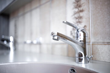 Shiny, chrome water tap inside apartment bathroom. Close up shot, shallow depth of field, no people