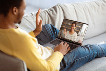 African american man having online party with his girlfriend, reclining on couch at home, using...