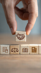 Hand positions wooden cube featuring handshake symbol above other cubes with business and legal icons
