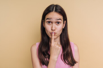 Young woman with long hair in pink top making a shushing gesture.