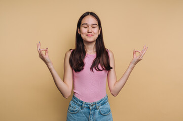 Young woman meditating with closed eyes against beige background.