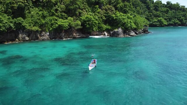 A fishing boat floats on turquoise waters off Pulau Nasi, Sumatra, Indonesia. The drone pulls back and ascends, unveiling the lush green coastline and the vibrant tropical sea.