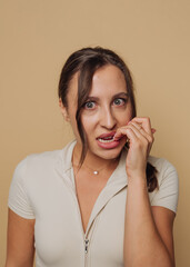 Woman biting nails with a worried expression against a beige background.