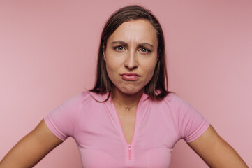 Fototapeta premium Woman in pink shirt with a frustrated expression against pink background.