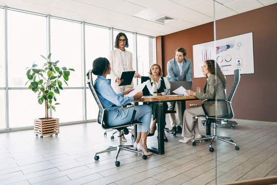 Professional business team collaborating in a modern office setting while discussing strategy and corporate goals around a workspace table