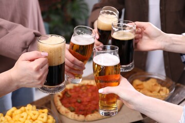 Friends clinking glasses of beer at wooden table, closeup