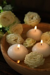 Burning candles, water and rose flowers in bowl on wooden table, closeup