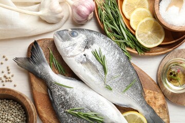 Fresh raw dorado fish, lemon slices, rosemary and spices on white wooden table, flat lay. Organic seafood