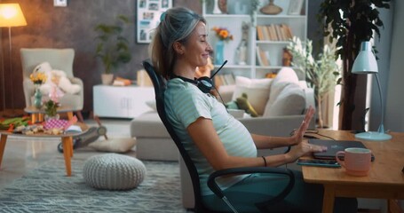 Satisfied pregnant woman closing laptop after finishing remote work at desk, leaning back to relax with a smile, enjoying accomplishment, while her daughter plays in the living room background. - Powered by Adobe