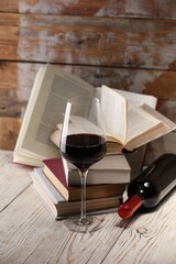 Red wine in glass, bottle and books on light table against color wooden background