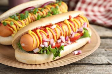 Delicious hot dogs with sauces, lettuce and onion on wooden table, closeup