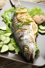 Tasty roasted seabass fish served with vegetables and lemon on wooden table, closeup. Homemade...