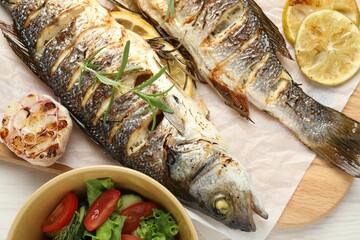 Tasty roasted seabass fish served with salad and lemon on white wooden table, top view. Homemade seafood dish