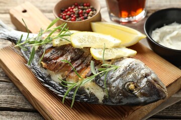 Tasty roasted dorado fish served with rosemary and lemon on wooden table, closeup. Homemade seafood...