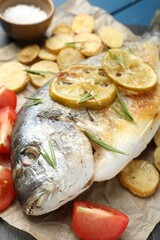 Tasty roasted dorado fish with vegetables and spices on table, closeup. Homemade seafood dish