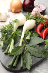 Different fresh herbs, garlic, onions and other spices on grey table, closeup