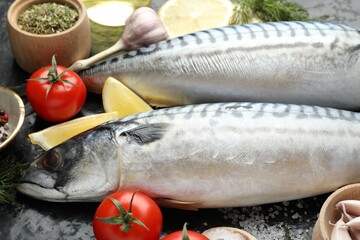 Fresh raw mackerels and spices on black table, closeup. Seafood delicacies
