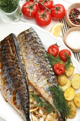 Tasty roasted mackerels with spices, tomatoes and potatoes on table, flat lay. Homemade seafood dish