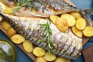 Tasty roasted mackerels with spices and potatoes on blue wooden table, flat lay. Homemade seafood dish