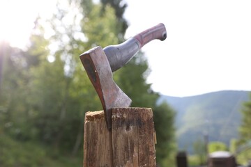 Metal axe on wooden log outdoors, closeup