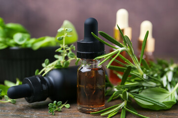 Bottles of aromatic essential oils and herbs on wooden table against brown background, closeup