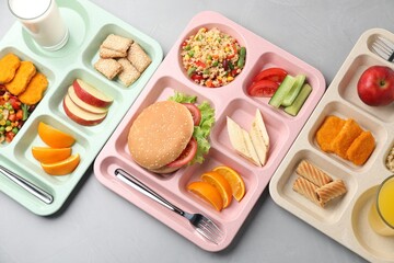 Plastic trays with tasty food, milk and orange juice on grey table, top view. School lunch
