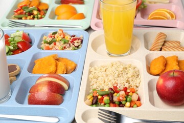Plastic trays with tasty food and orange juice on table, closeup. School lunch
