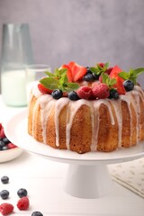 Delicious bundt cake with berries, glaze and mint on white wooden table against grey background, closeup
