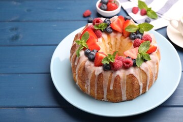 Delicious bundt cake with berries, glaze and mint on blue wooden table, closeup