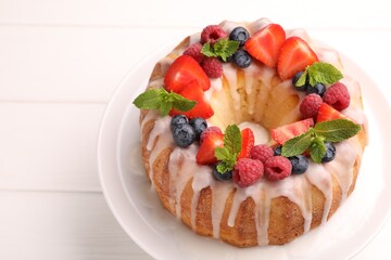 Delicious bundt cake with berries, glaze and mint on white wooden table, closeup