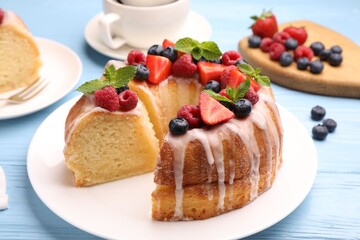 Pieces of delicious bundt cake with berries, glaze and mint on light blue wooden table, closeup