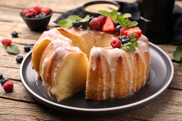 Pieces of delicious bundt cake with berries, glaze and mint on wooden table, closeup
