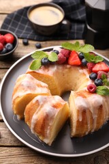 Pieces of delicious bundt cake with berries, glaze and mint on wooden table, closeup